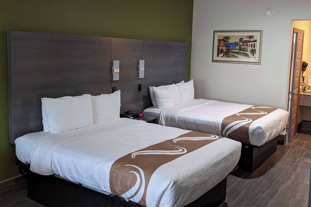 Une chambre d’hôtel avec deux lits, une table de chevet, une lampe fixée au mur et un tableau.