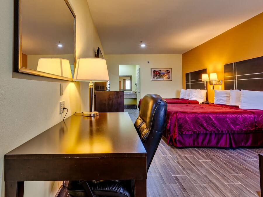 Habitación de hotel con escritorio, una silla, cama con ropa de cama roja, un espejo grande y dos lámparas fijadas a la pared.
