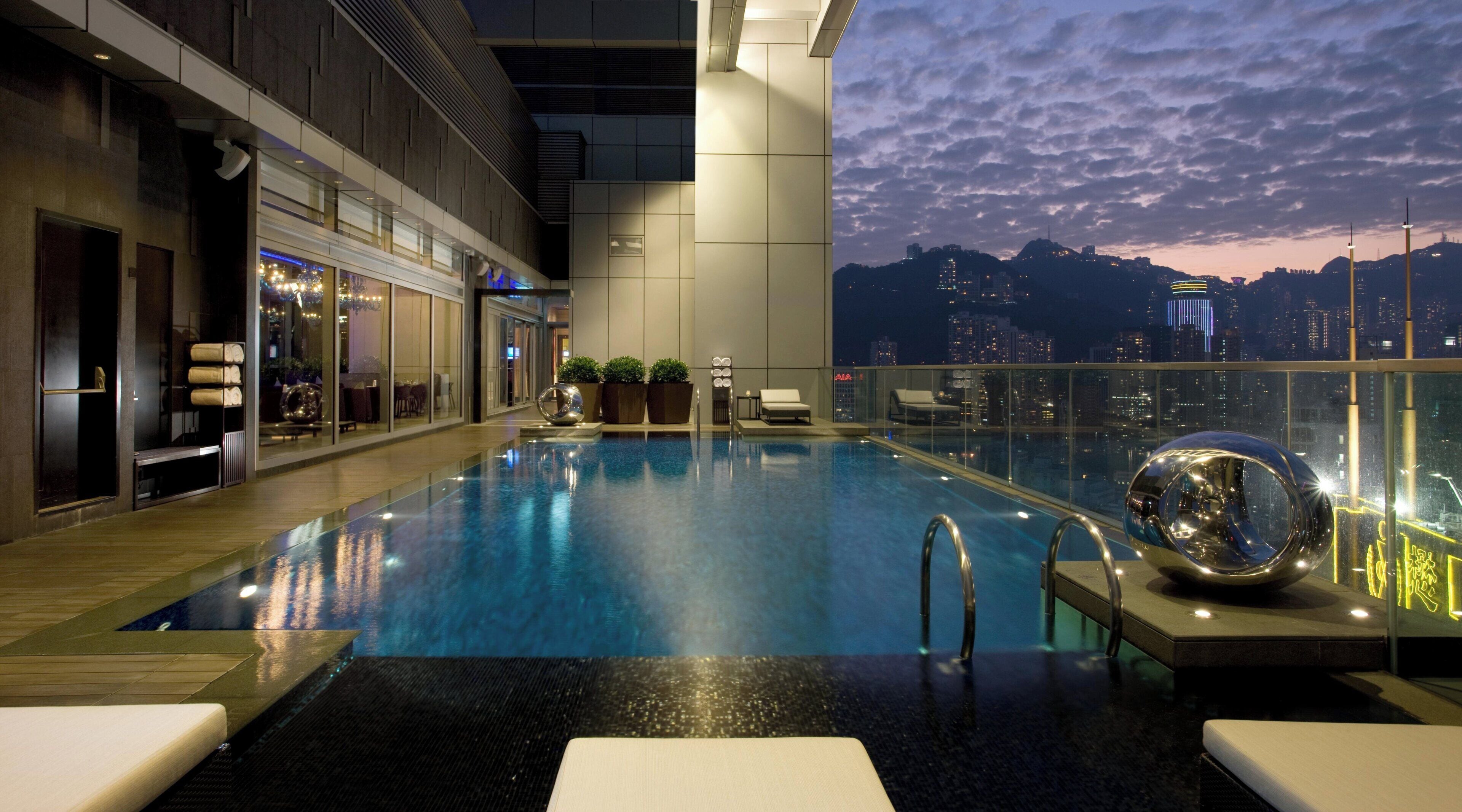 An indoor infinity pool with a city view, lounge chairs, and a modern interior design.