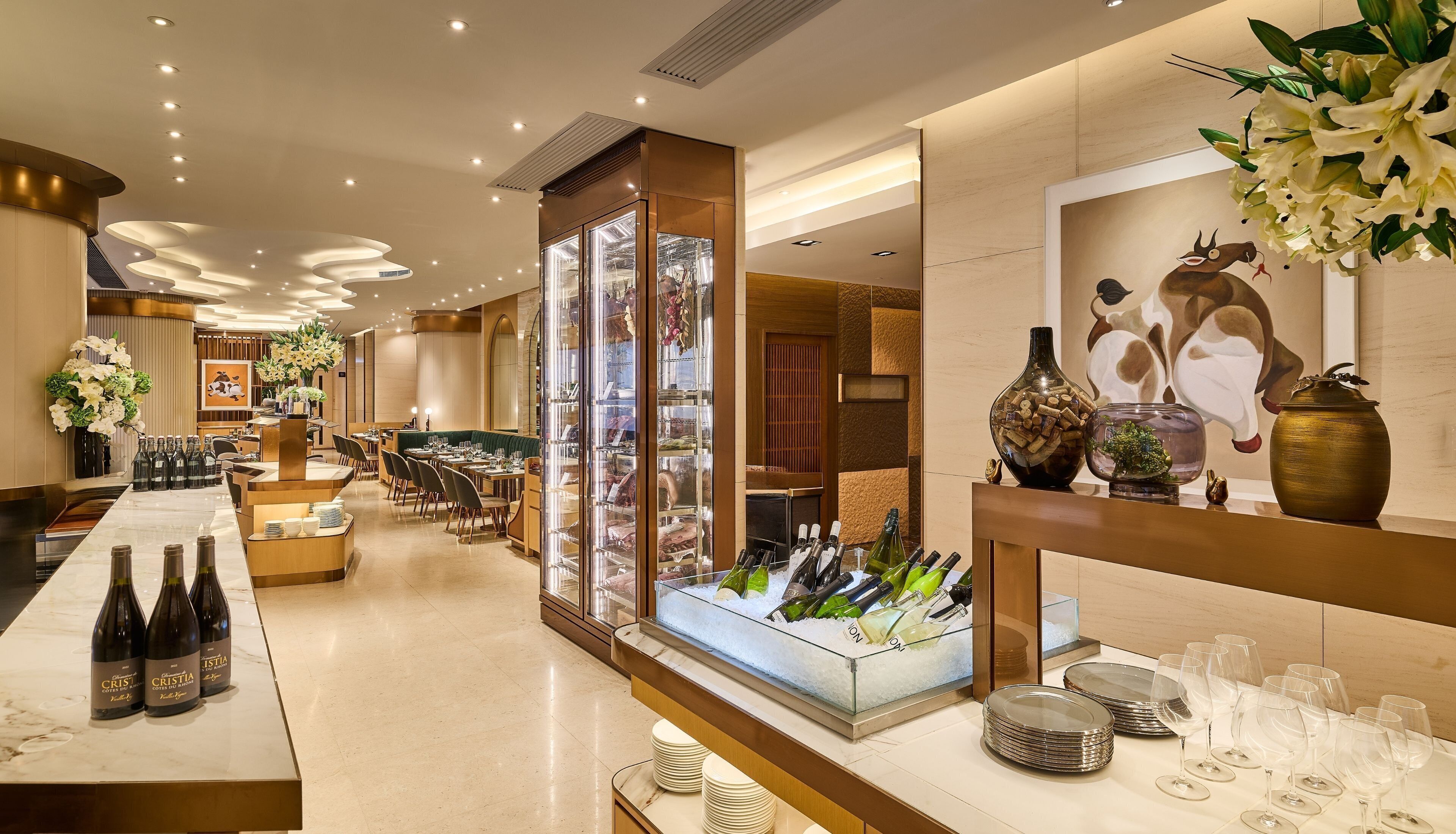 A hotel lobby with a reception desk, seating area, and a display of wine bottles and glasses.