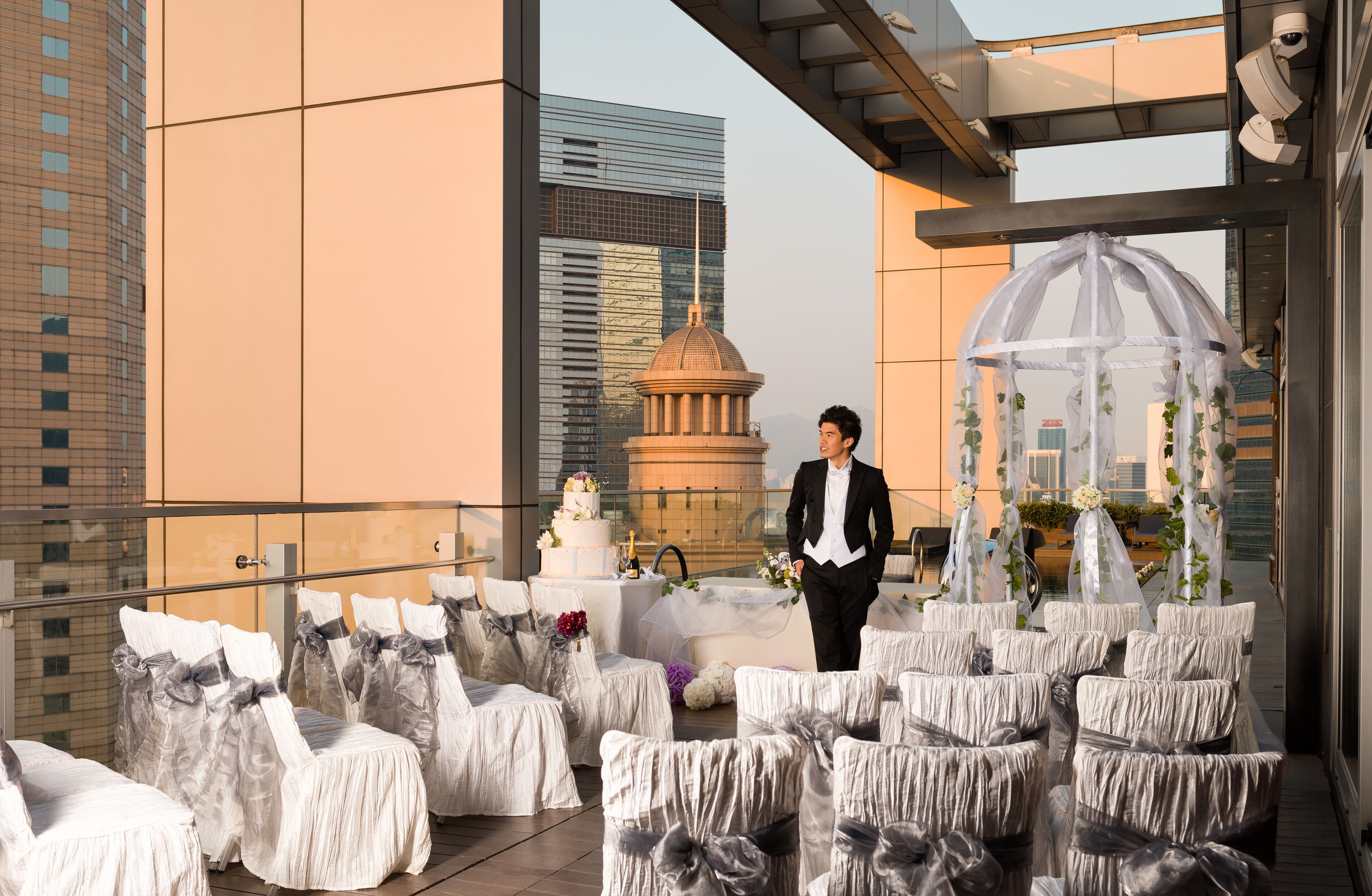 A rooftop wedding setup with covered chairs, a wedding cake, and a gazebo.