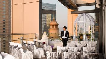 A rooftop wedding setup with covered chairs, a wedding cake, and a gazebo.