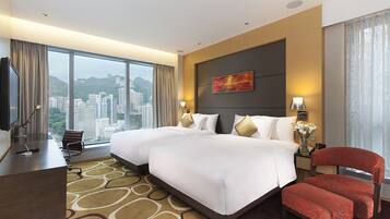 A hotel room with two beds, a desk, a chair, and a large window offering a city view.