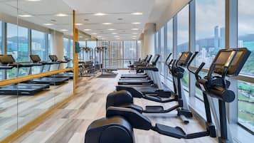 A gym with treadmills, elliptical machines, and weight benches, large windows with a city view.