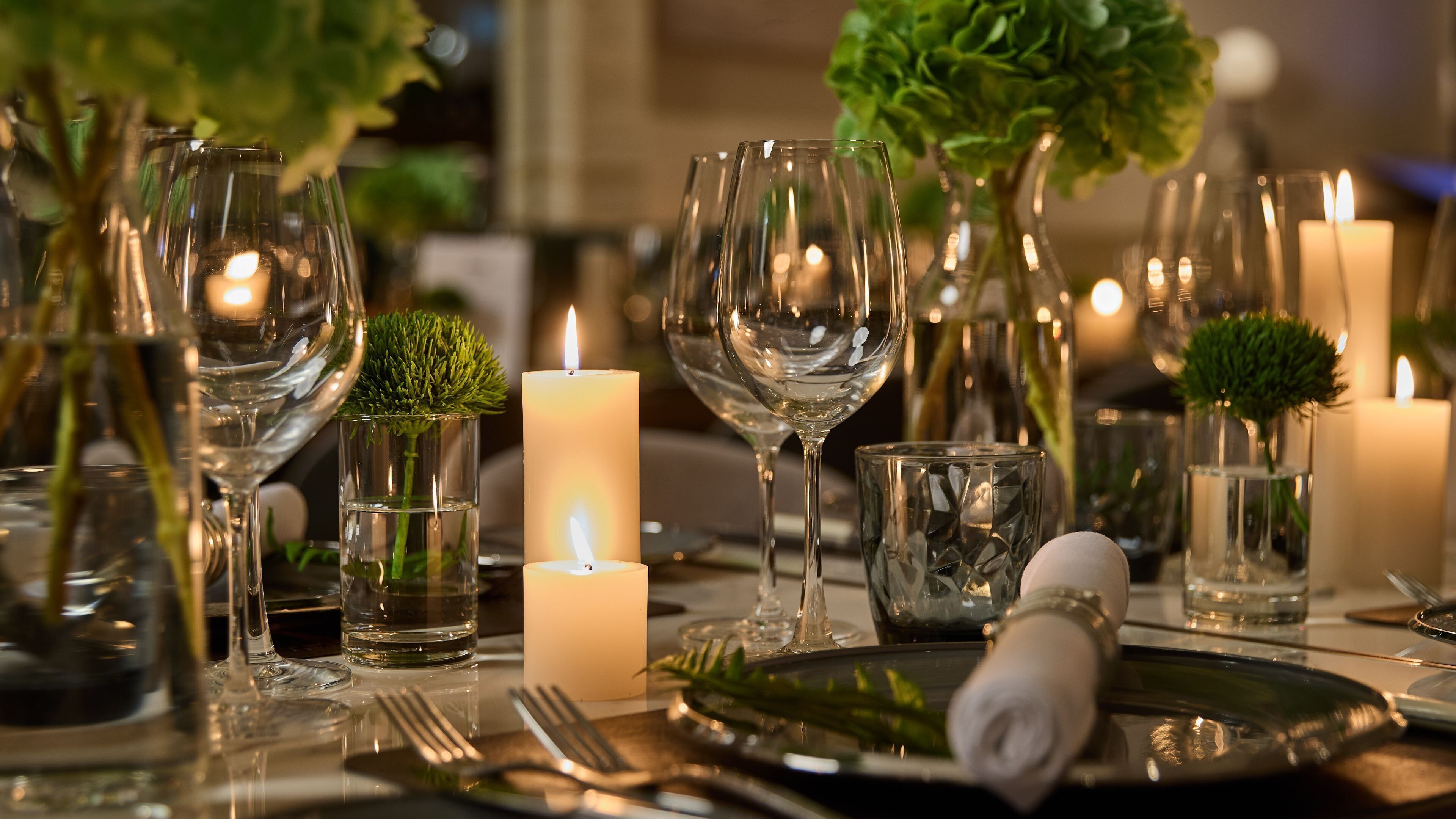 A table set with wine glasses, candles, and greenery.