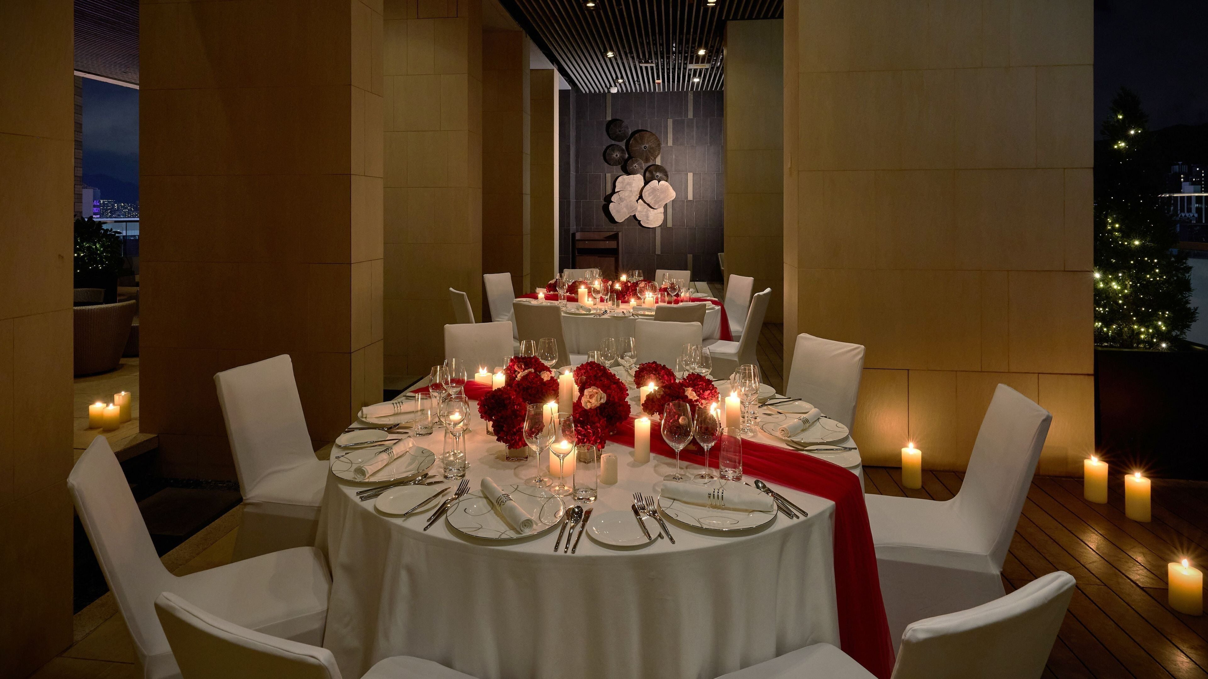 A formal dining area with round tables, white chairs, and red floral centerpieces.