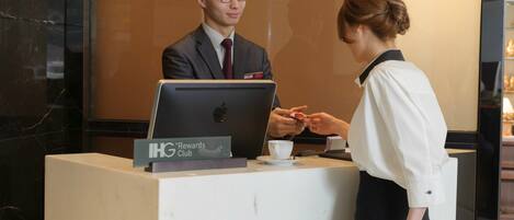 A reception desk with a laptop, a name tag, and a sign for the IHG Rewards Club.