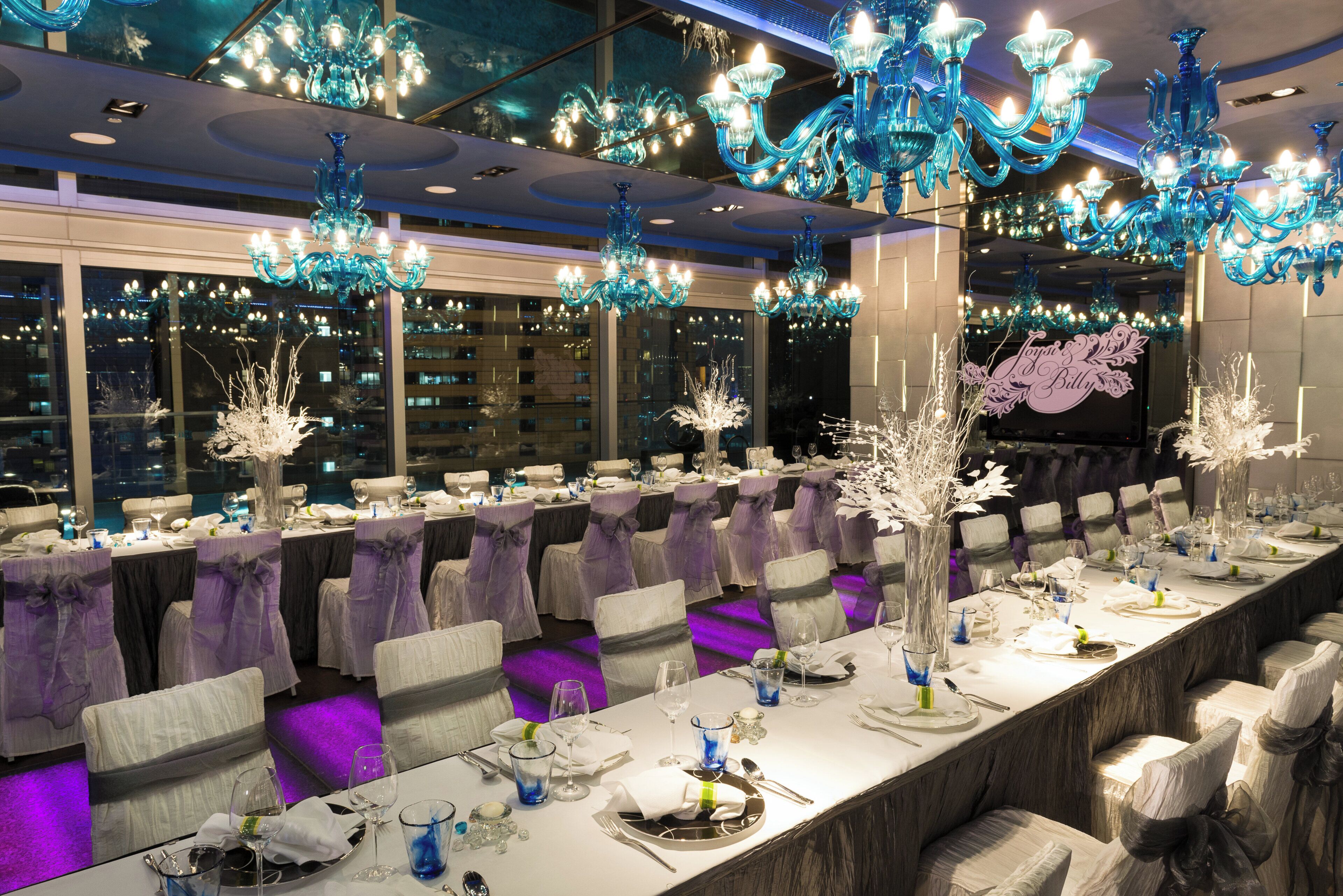 Een feestzaal met lange tafels, stoelen en decoratieve glazen kroonluchters.