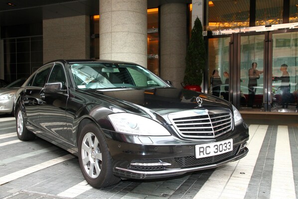A black luxury sedan parked in front of a building with large columns and a glass entrance.
