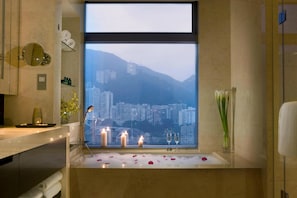 A bathroom with a bathtub, candles, and a view of a cityscape through a large window.