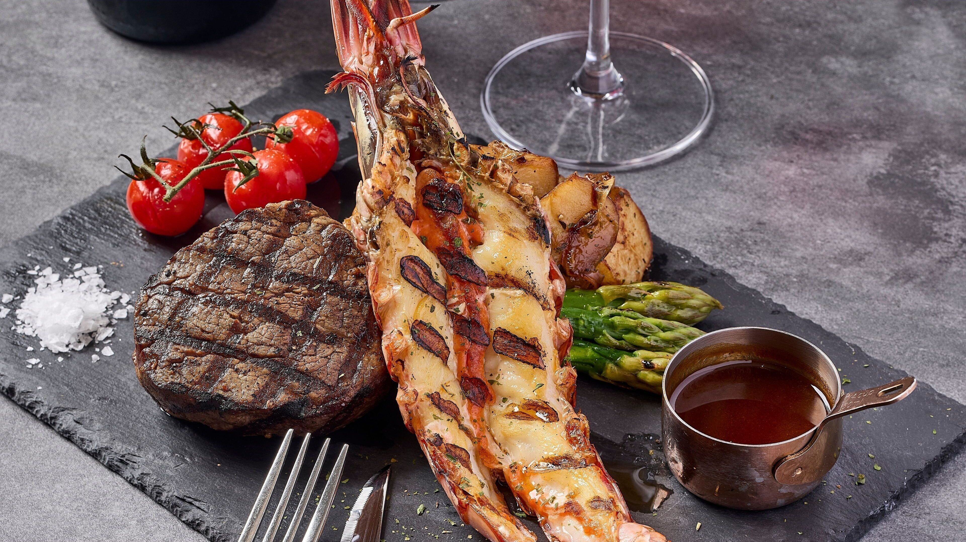 A meal with grilled meat, asparagus, and a glass of red wine on a slate board.