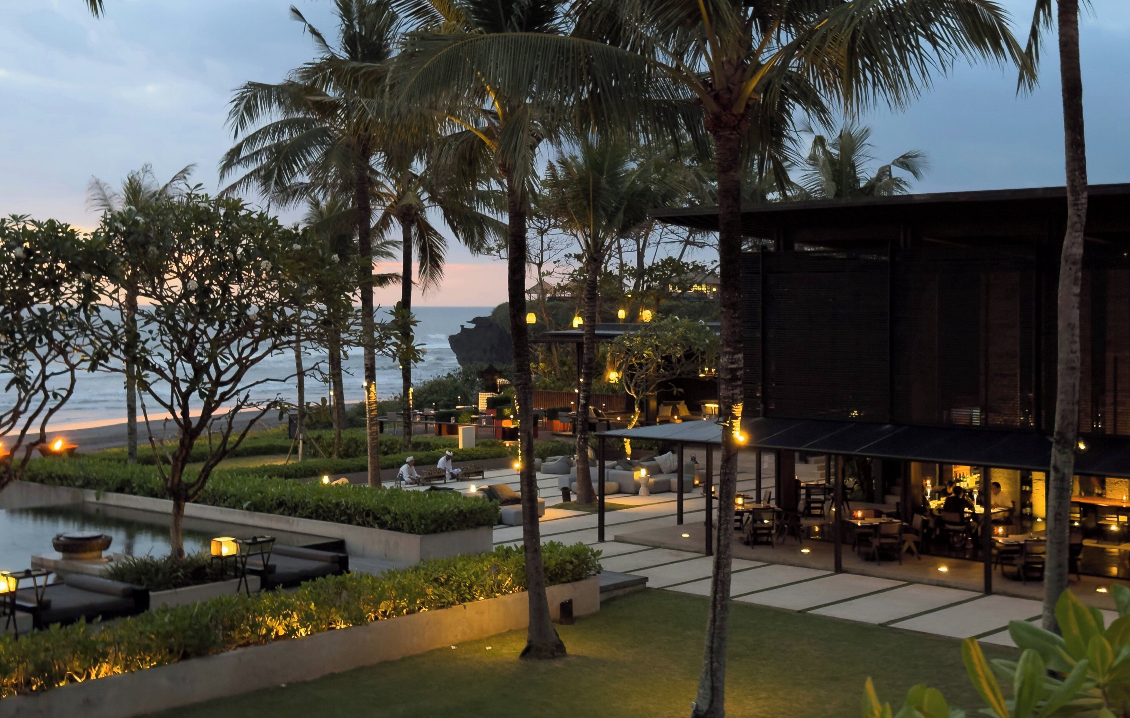 A resort with outdoor seating, palm trees, and a view of the ocean.
