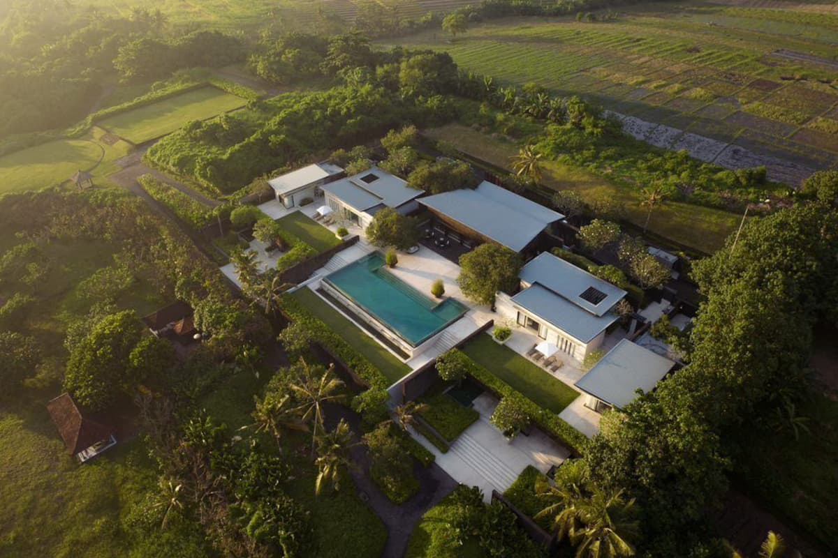 An aerial view of a property with multiple buildings, a swimming pool, and surrounding lush greenery.