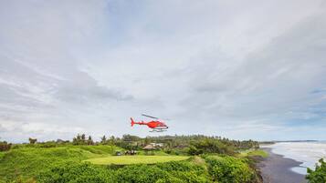 A red helicopter flying over a lush green landscape with a beach in the background.