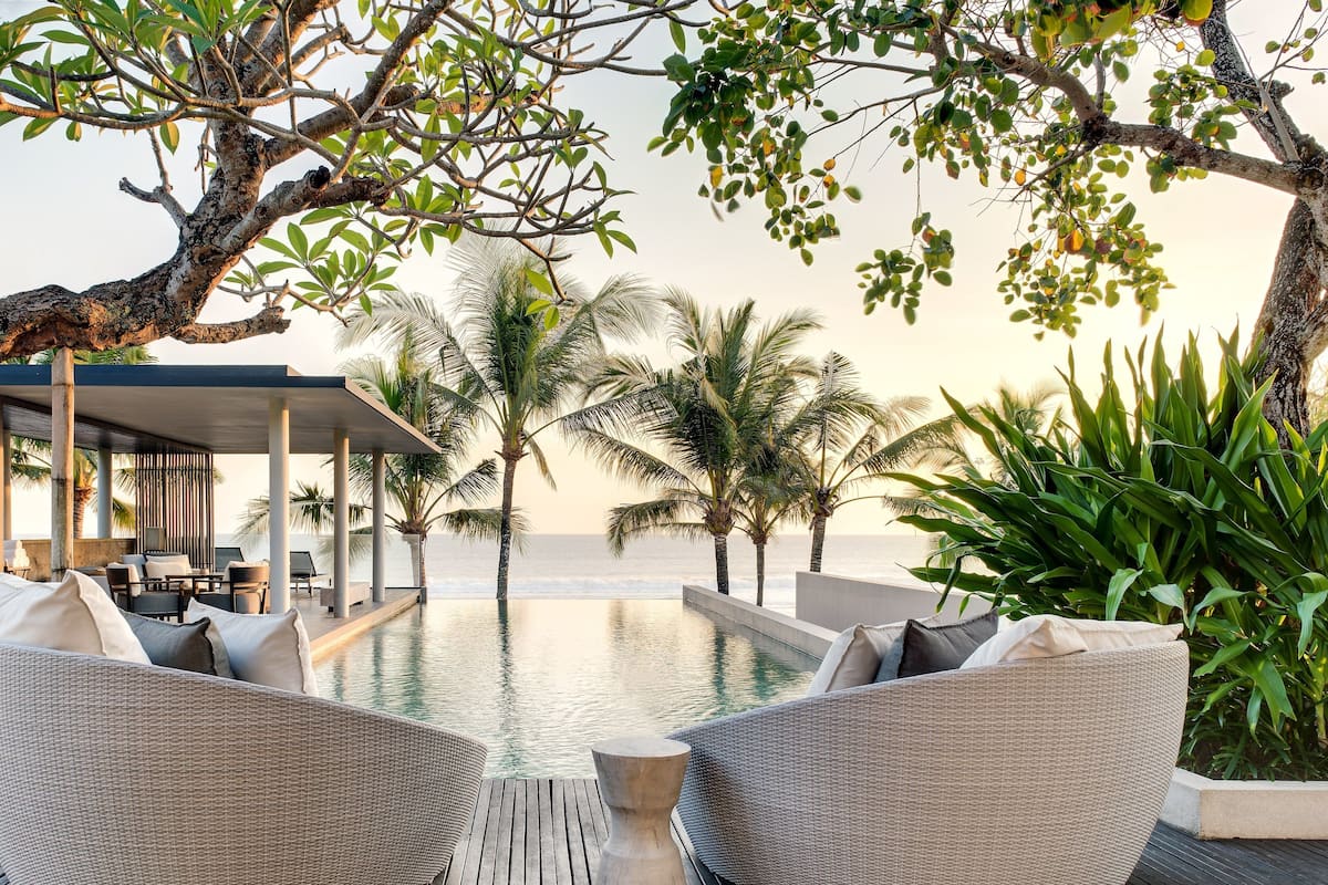 A poolside area with wicker furniture and a view of the ocean.