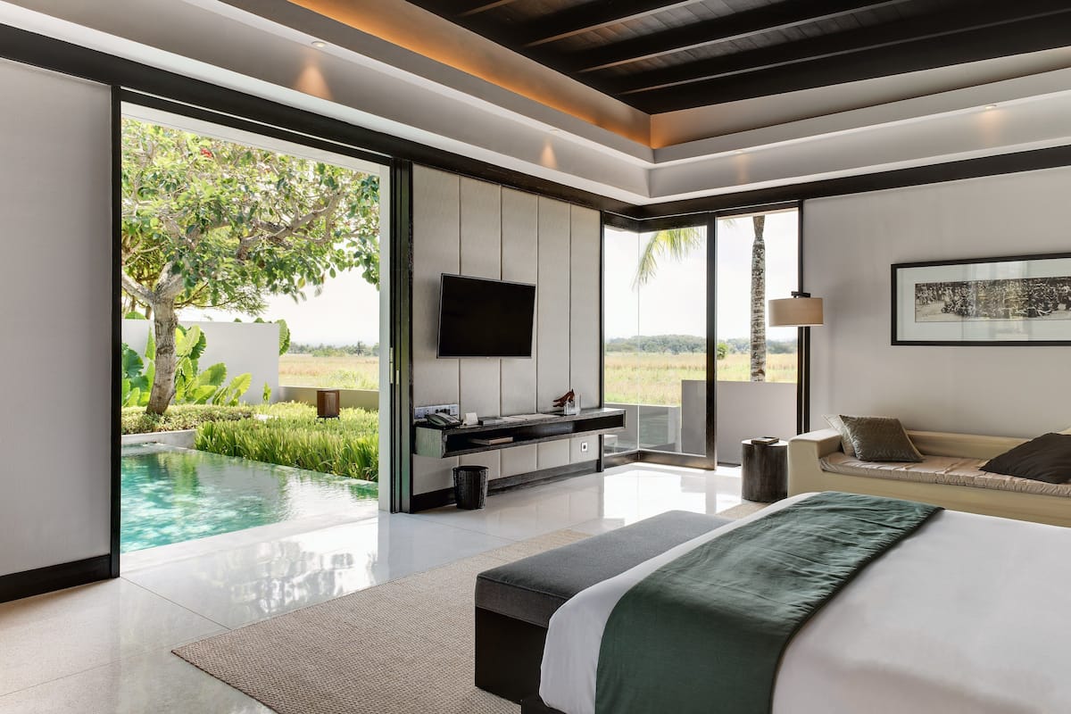 A modern bedroom with a large bed, a TV, a sofa, and a view of a swimming pool.