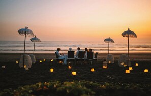 Un espace de restauration aménagé sur la plage, avec des tables et des chaises, entouré de lanternes décoratives et de parasols.