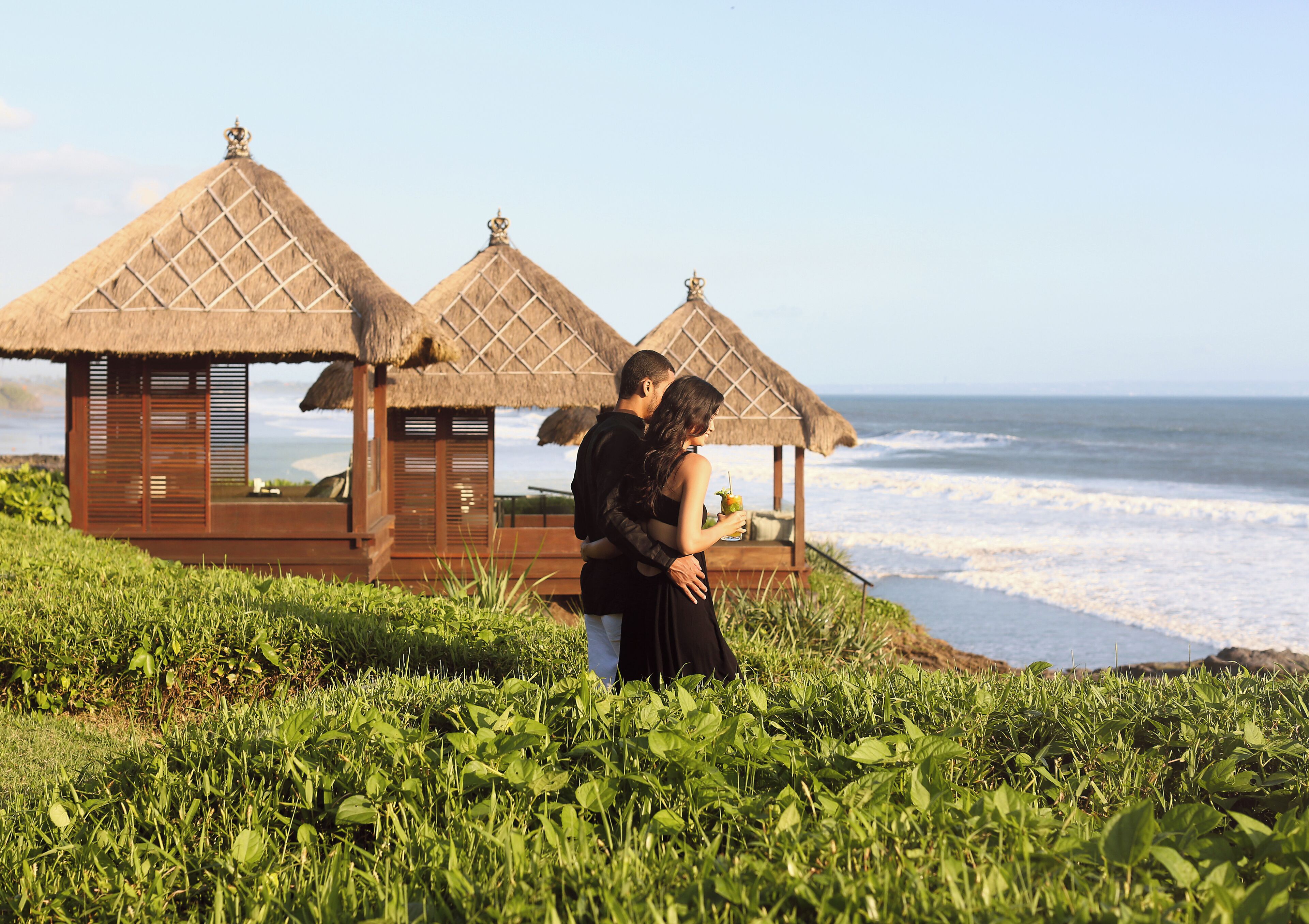 Un couple se tient devant une petite cabane au bord de la plage, avec vue sur l’océan.