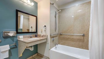 A bathroom with a sink, mirror, vanity, and a shower with grab bars.