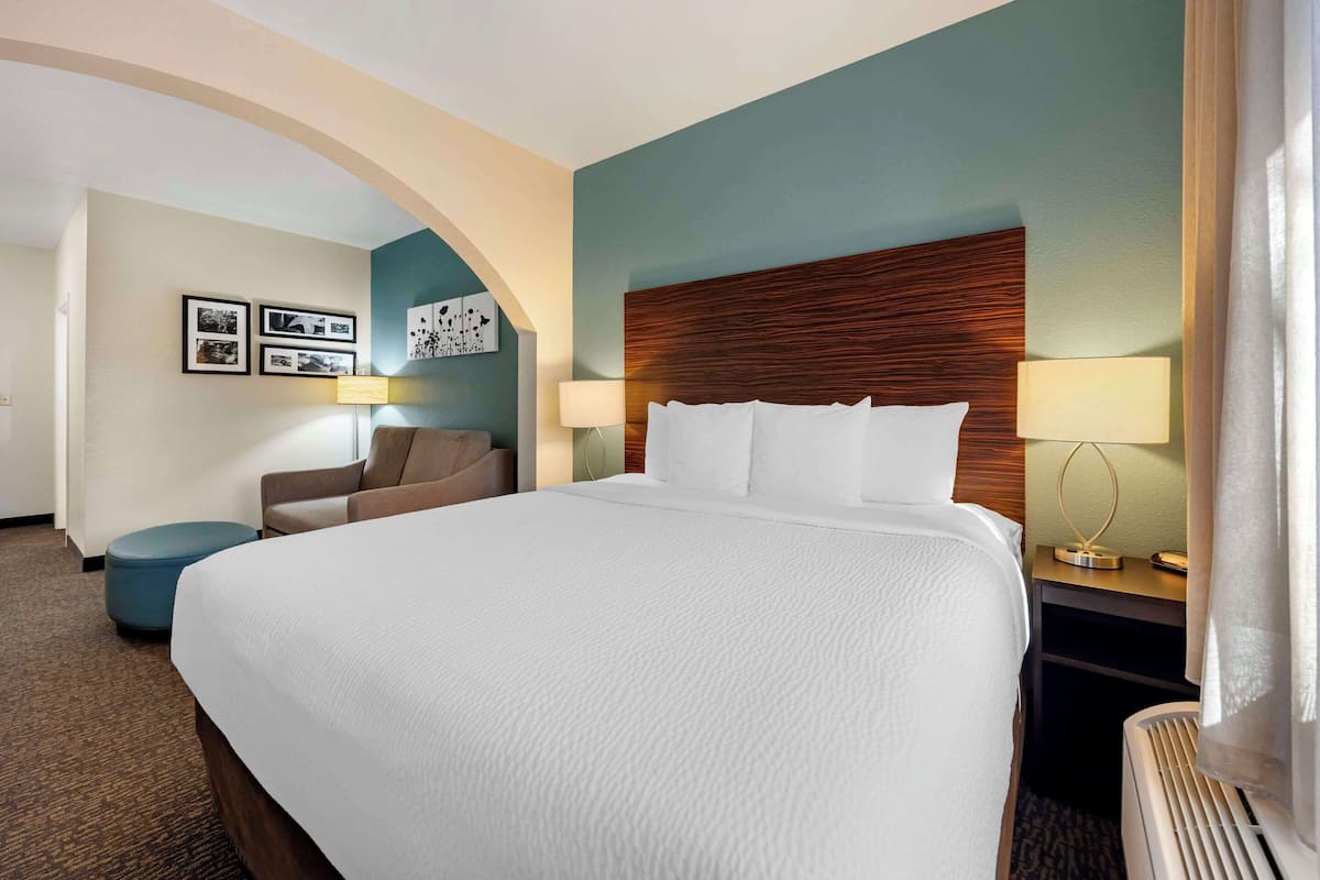 A hotel room with a large bed, two bedside lamps, a desk with a lamp, a chair, and a small ottoman.