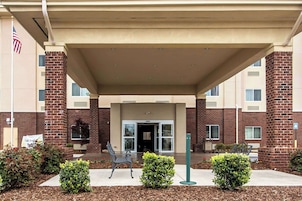A building entrance with a covered walkway, a flag, and a bench.