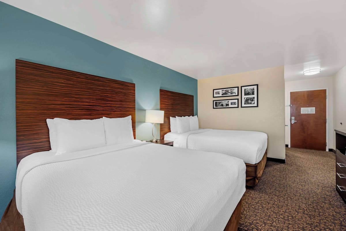 A hotel room with two beds, a wooden headboard, a lamp, and framed pictures on the wall.