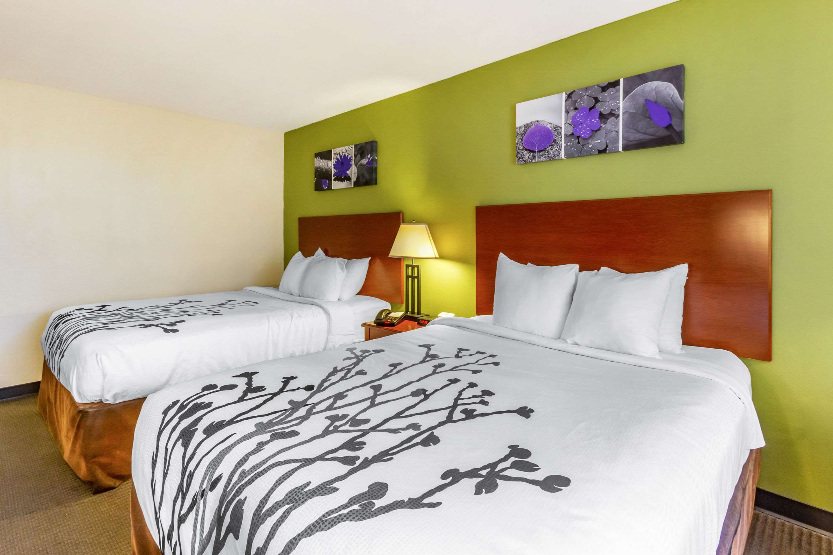 A hotel room with two beds, a nightstand, a lamp, and artwork on the walls.