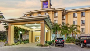Ett Sleep Inn & Suites-hotell med en ingång under tak, palmer och en parkeringsplats för stora terrängbilar.