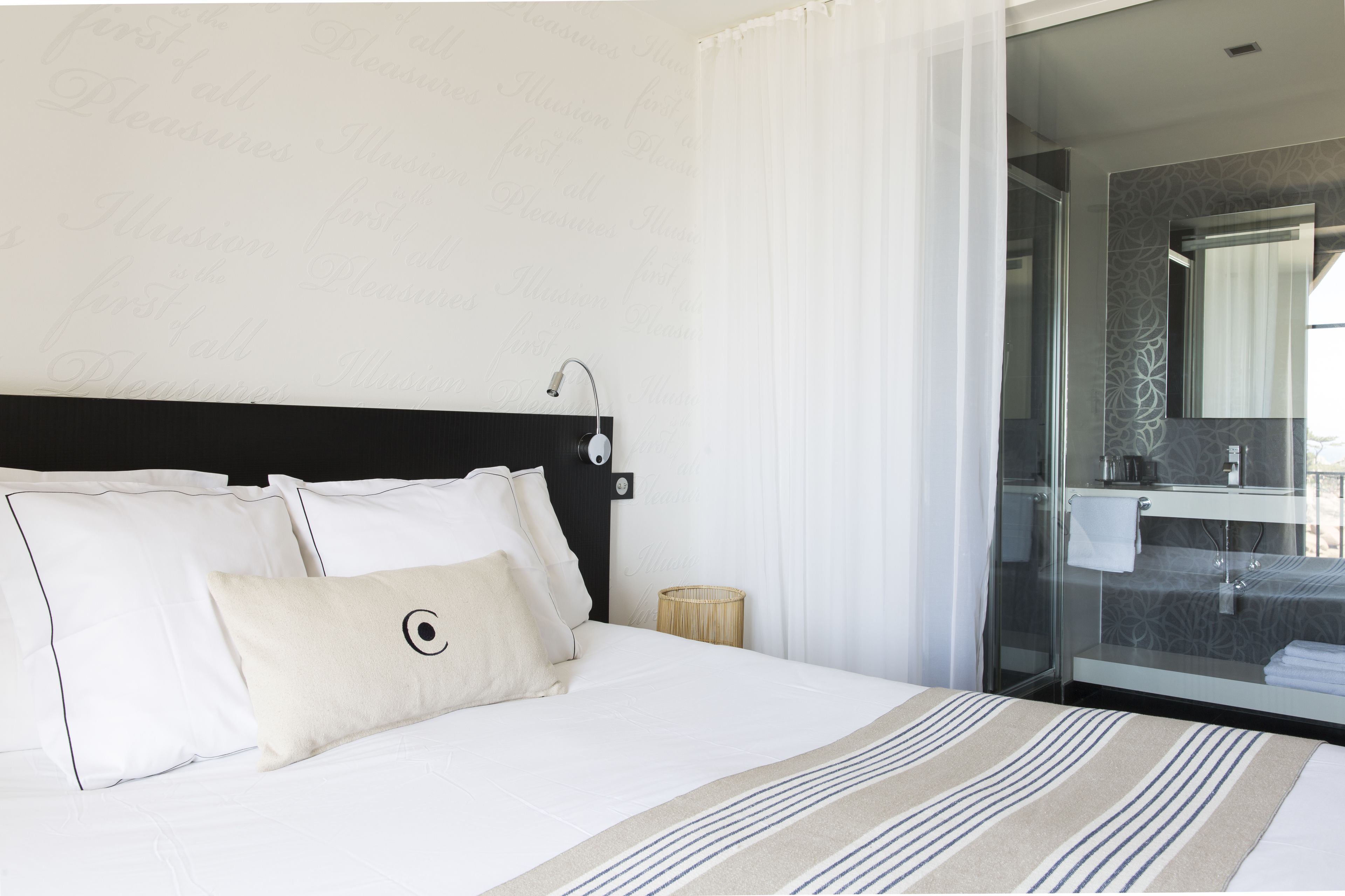 Een hotelkamer met een bed, nachtkastje, lamp en een badkamer zichtbaar door een glazen deur.