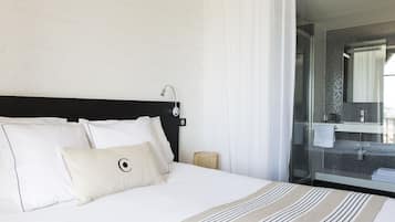 Een hotelkamer met een bed, nachtkastje, lamp en een badkamer zichtbaar door een glazen deur.
