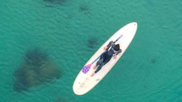 An aerial view of a person lying on a surfboard in clear turquoise water.