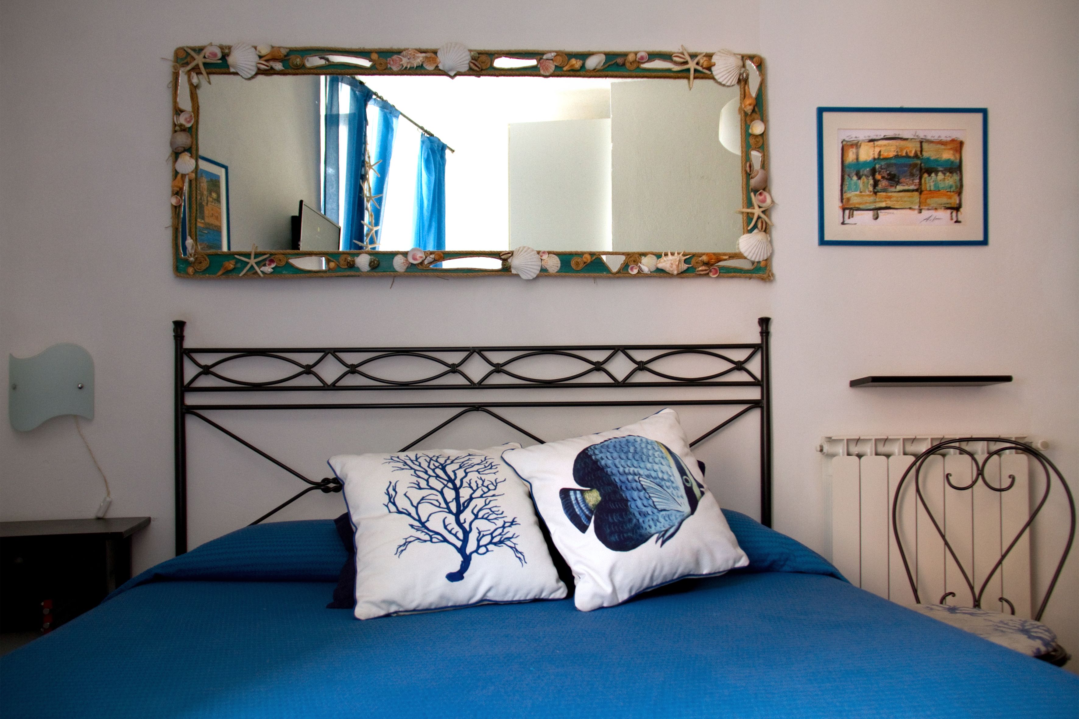 Ein Schlafzimmer mit einem Bett, zwei Kissen, einem Wandspiegel, einem gerahmten Bild und einer Heizung.