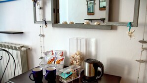 A room with a wooden table, two blue mugs, a clear box with items, a silver kettle, and a mirror with shells on the wall. - Rollando Affittacamere (Vernazza)