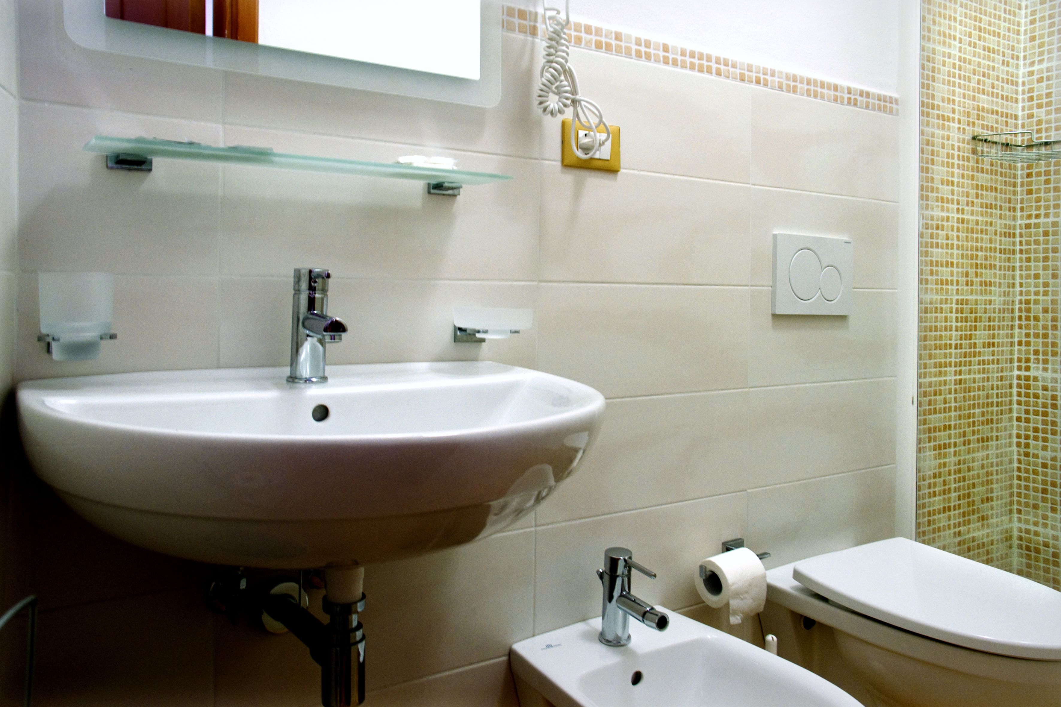 A bathroom with a sink, toilet, and glass shelf.