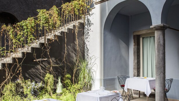 Un espace extérieur aménagé pour les repas, avec des tables et des chaises, un escalier et de la verdure.