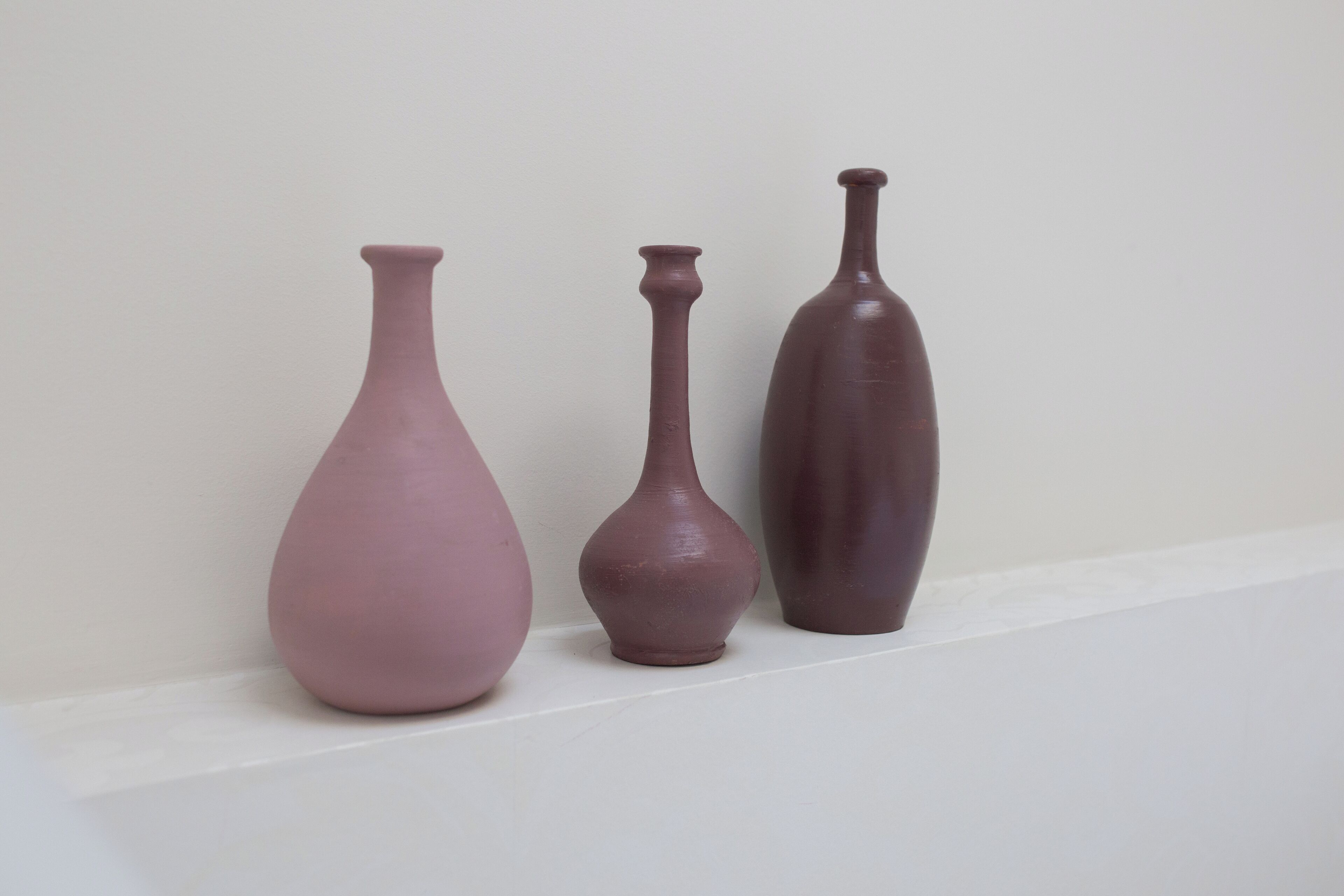 Three ceramic vases of varying sizes and shapes on a white shelf against a plain wall.