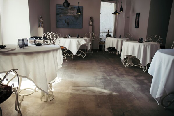 Un comedor con mesas redondas cubiertas con manteles blancos, sillas de metal e iluminación colgante.