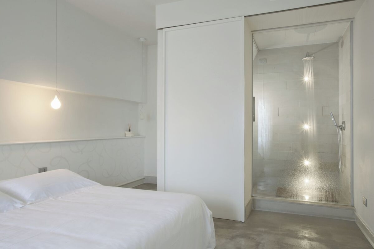 A modern bedroom with a bed, a wardrobe, and a glass-enclosed shower area.