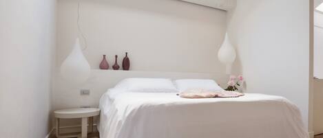 Quarto com claraboia, uma cama, mesas de cabeceira e vasos decorativos.