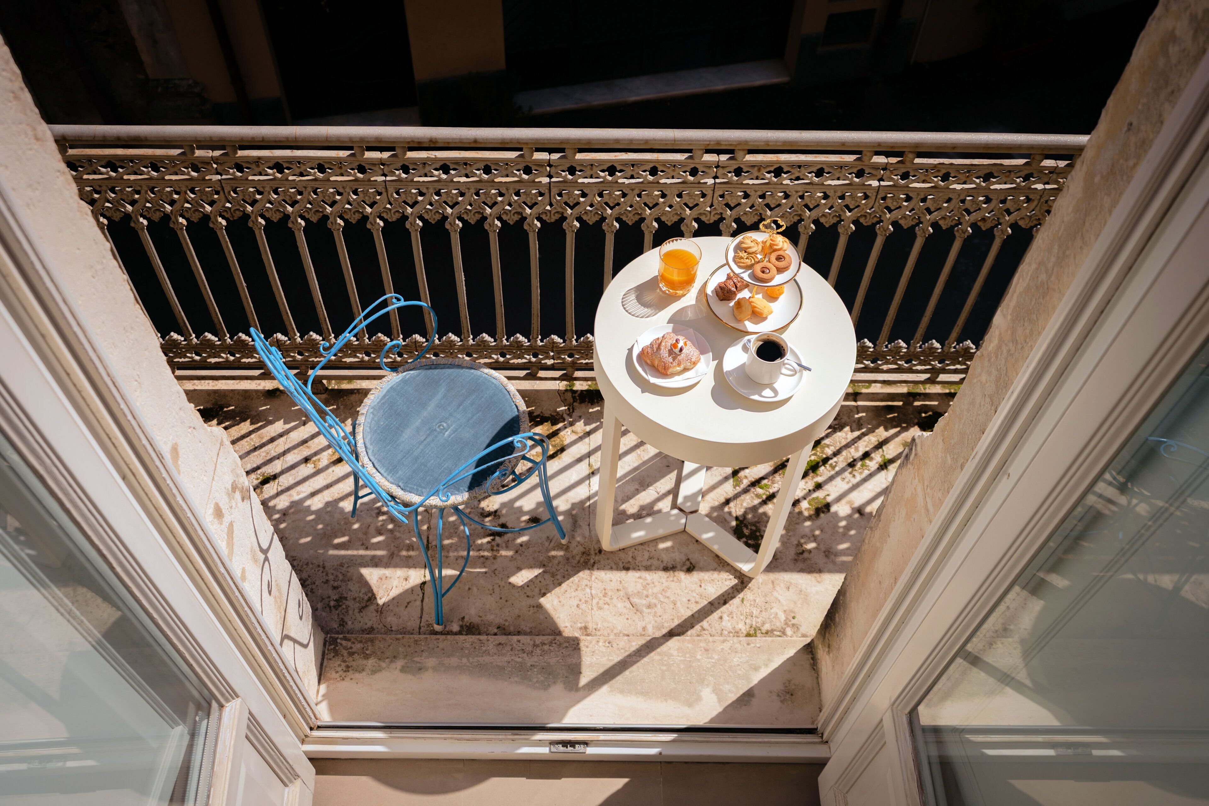 A balcony with a table set for breakfast, including pastries, coffee, and orange juice.