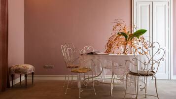 Uma área de refeições com uma mesa, cadeiras, um vaso com flores e uma porta ao fundo.