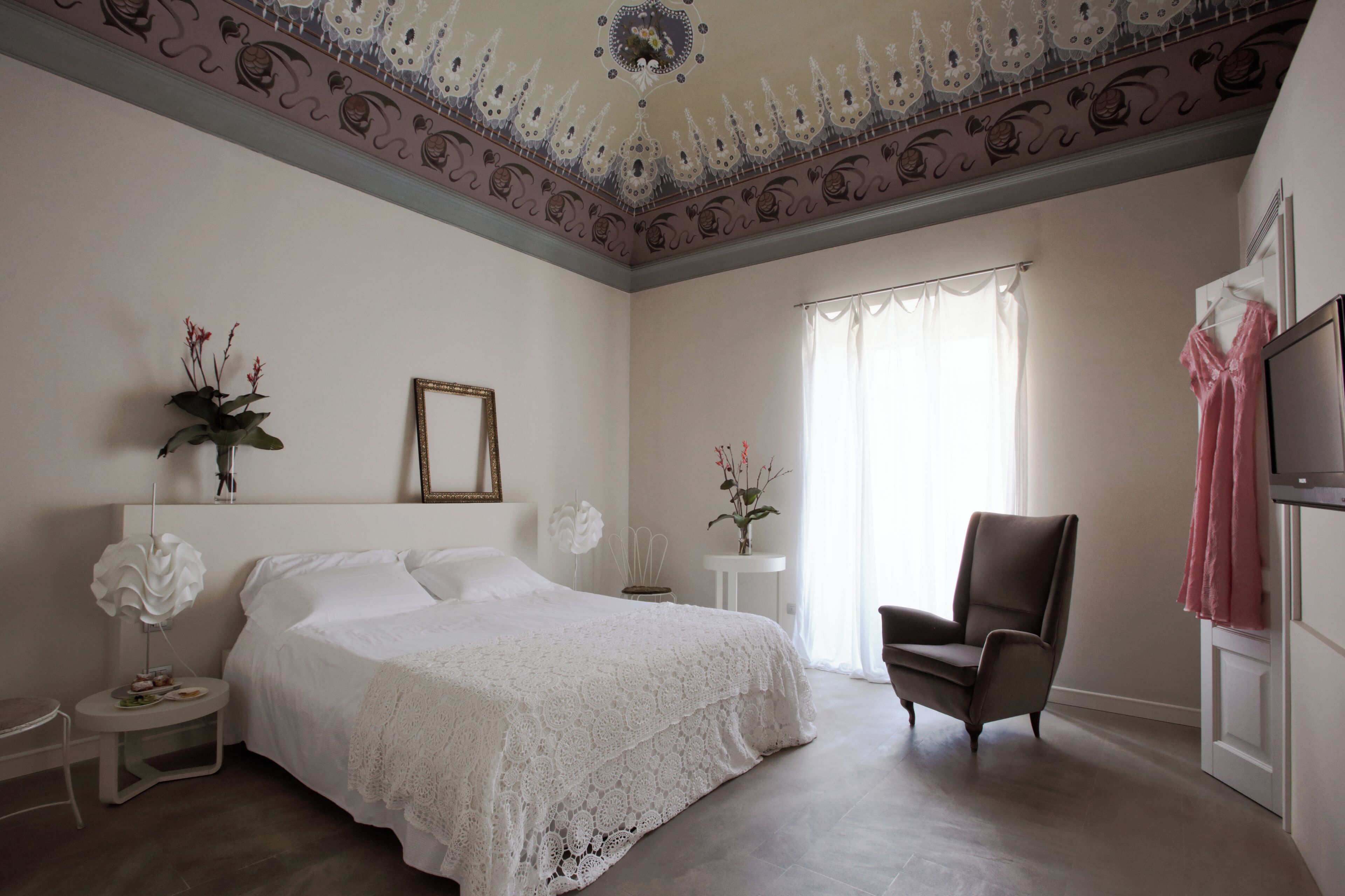 A bedroom with a large bed, a chair, a TV, and a window with curtains.