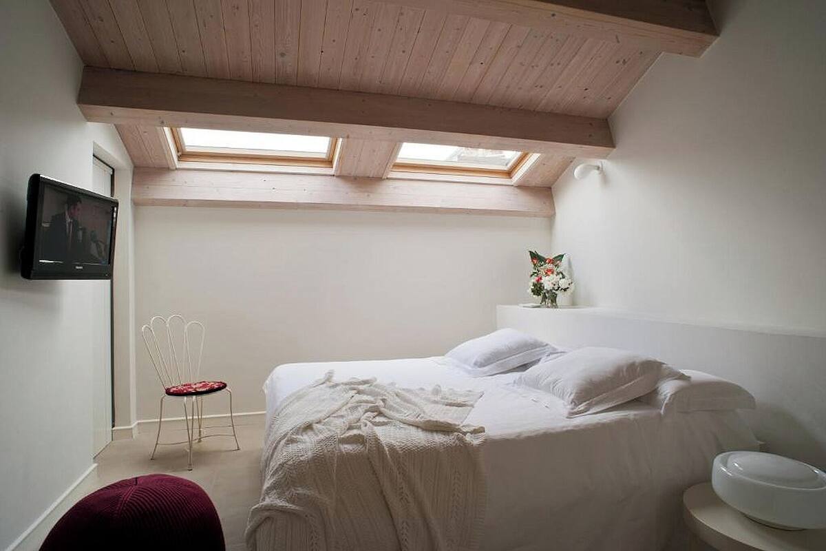 A bedroom with a bed, a chair, a TV, and a skylight.