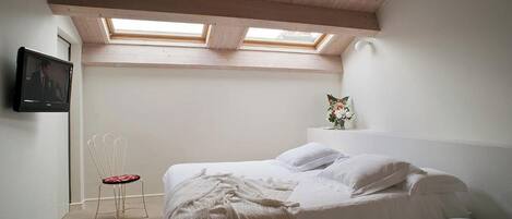 Une chambre à coucher avec un lit, une chaise, une télévision et une fenêtre de toit.