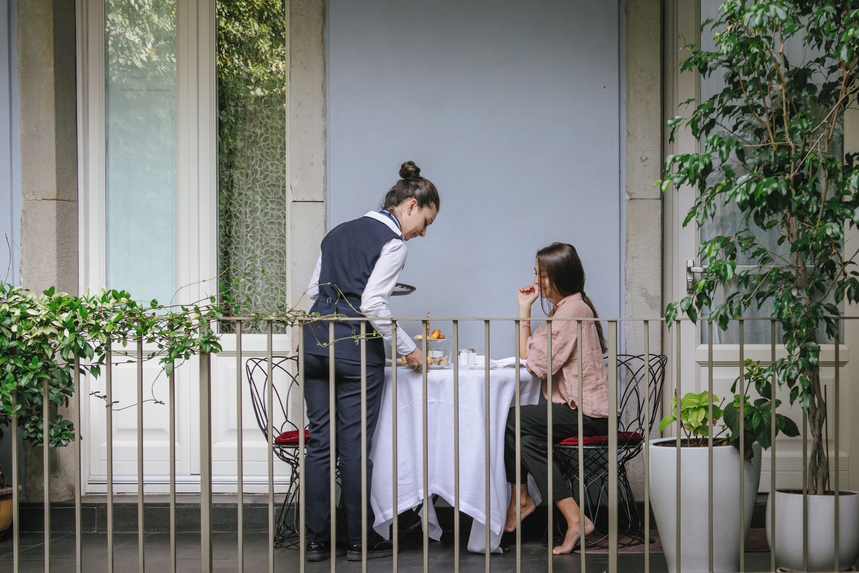 An outdoor dining area with a table set for two, a waiter, and a guest.