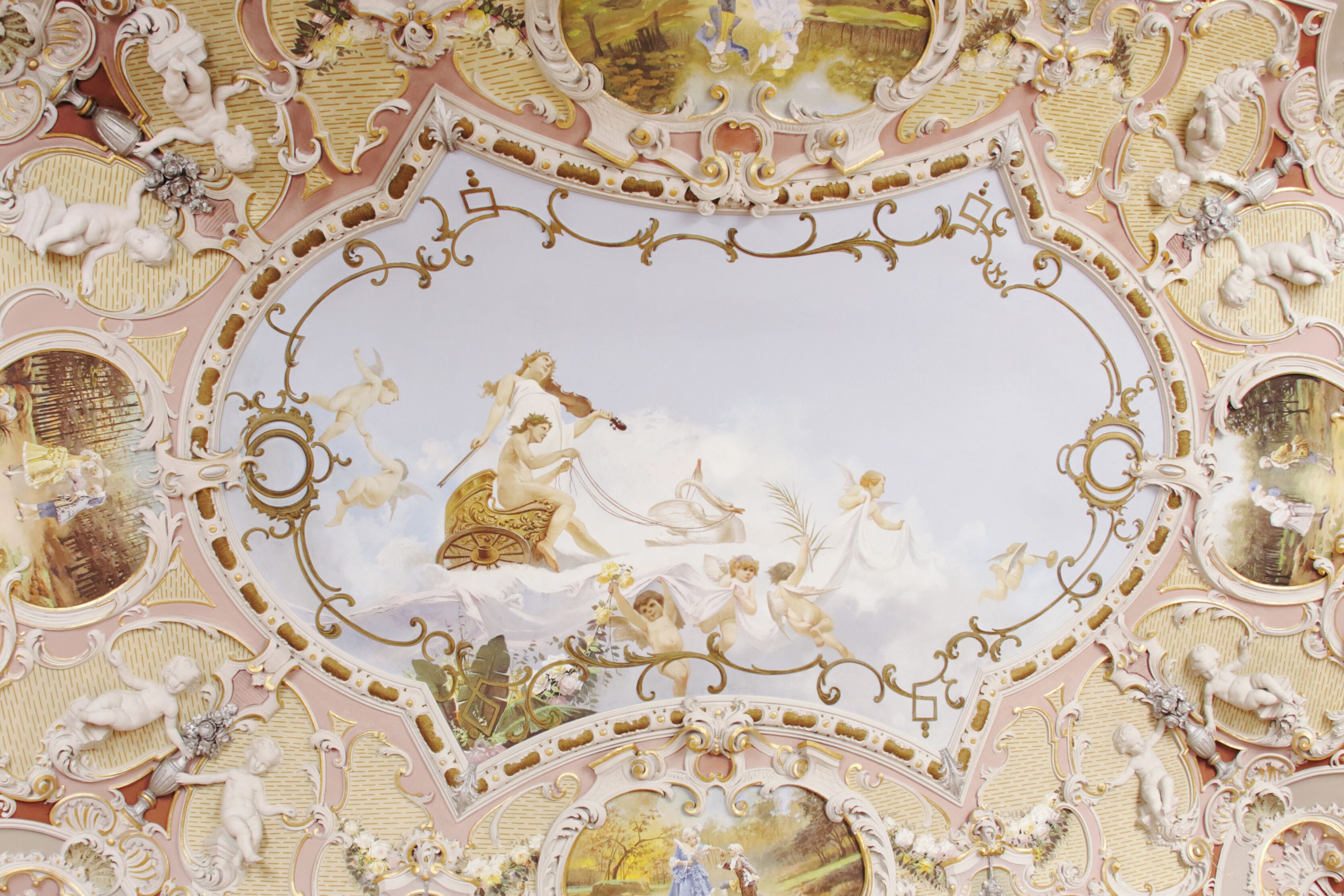 Un plafond orné de motifs dorés et blancs, comprenant des putins et des motifs floraux.
