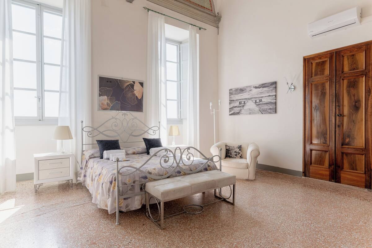 A bedroom with a bed, bench, bedside table, lamp, and artwork.