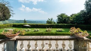A terrace with a view of a manicured garden and distant hills.