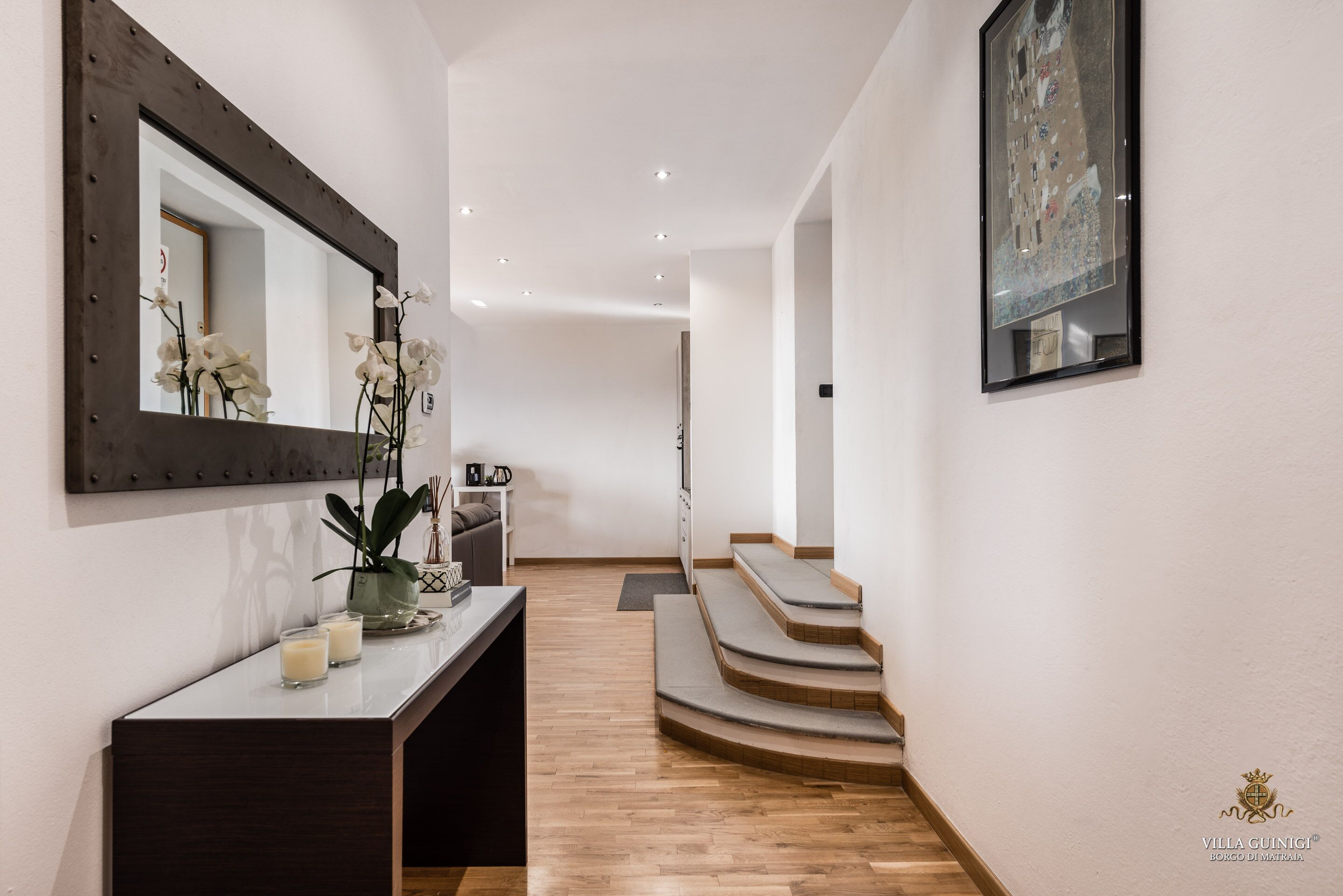 A modern hallway with a wooden floor, a dark console table with candles, a mirror, and a staircase leading to another room.