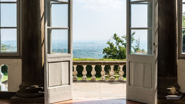 A room with large windows, a balcony with a balustrade, and a view of a landscape.